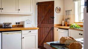 A kitchen with white cabinets, a wooden door, a bread box, and a loaf of bread on the counter. - Yew Tree Cottage | Farm Stay | Sleeps 4 (West Ayton)