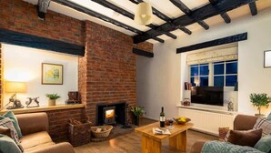 A cozy living room with a brick fireplace, wooden furniture, and a large window. - Yew Tree Cottage | Farm Stay | Sleeps 4 (West Ayton)