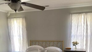 A bedroom with a bed, a dresser, a ceiling fan, and sheer curtains.