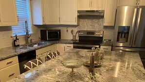 A kitchen with white cabinets, a granite countertop, stainless steel appliances, and a window with blinds.