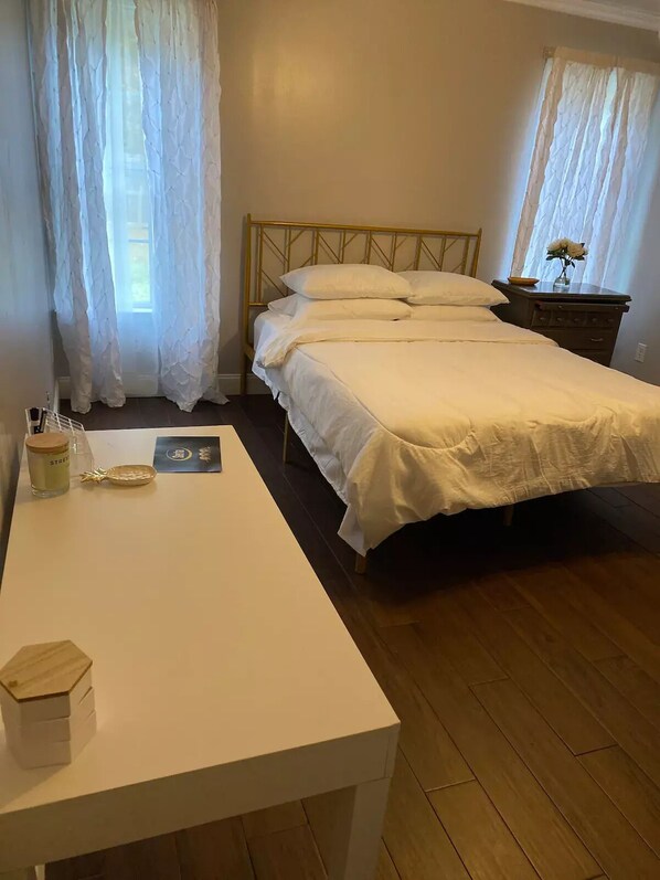 Une chambre à coucher avec un lit, une table de chevet, une commode et une fenêtre avec des rideaux.