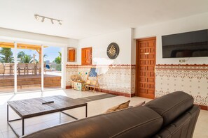 Un salon avec un canapé en cuir, une table basse en bois, un jeu de fléchettes et un téléviseur fixé au mur.