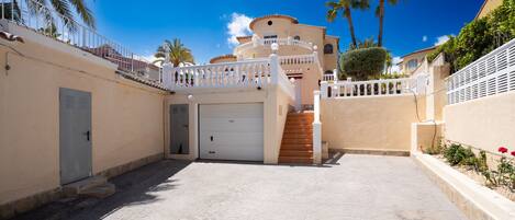 A residential building with a white balcony, a garage, and a paved driveway.