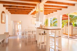 A spacious room with wooden beams on the ceiling, white chairs, and a dining table.