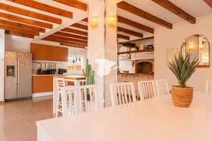 Une cuisine spacieuse avec des poutres en bois, un coin repas avec des chaises blanches et une grande plante en forme de cactus.