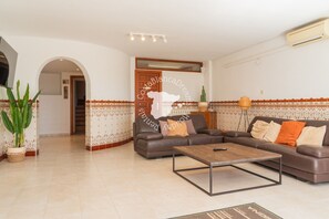 A living room with a sofa, coffee table, and a TV. There is a staircase leading to another room.