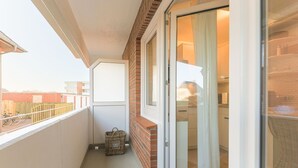 A narrow balcony with a wicker basket, a sliding glass door leading to a kitchen, and a view of the outside. - Appartement Northland 8 (Sylt)