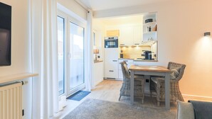 A modern kitchen with white cabinets, a dining table with wicker chairs, and a built-in oven. - Appartement Northland 8 (Sylt)