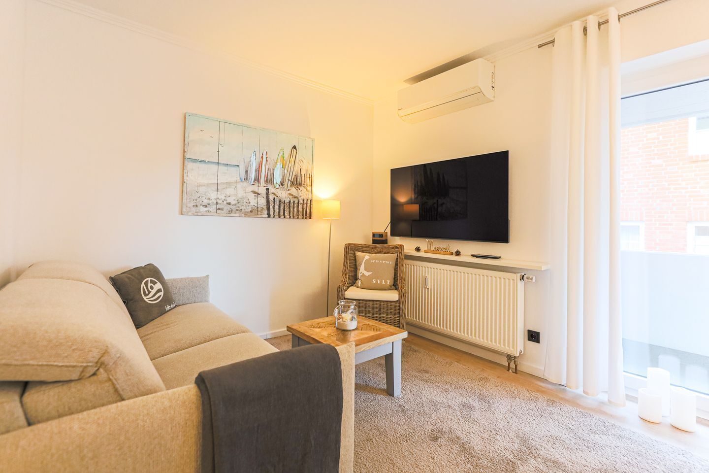 Un salon avec un canapé, une table basse, un téléviseur, un radiateur et une fenêtre avec des rideaux.
