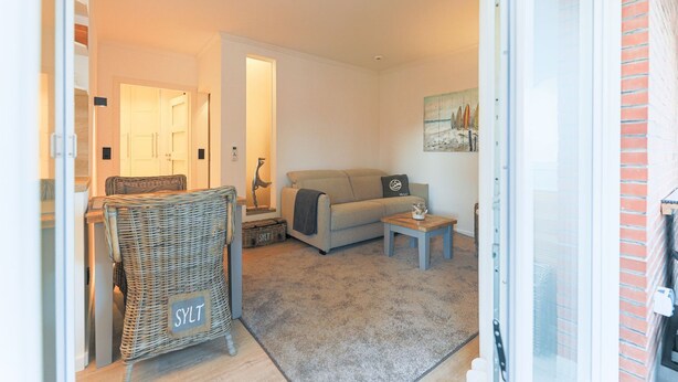 A cozy living room with a sofa, a wicker chair, and a small table. - Appartement Northland 8 (Sylt)