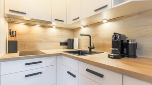 A modern kitchen with white cabinets, a wooden countertop, a Bosch range hood, a sink with a black faucet, and a coffee machine. - Appartement Northland 8 (Sylt)