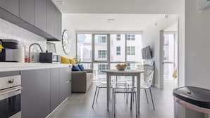 A modern kitchen with grey cabinets, a dining area with a white table and chairs, and a large window offering a city view. - MirabileCondoDwntown MIA Brickell w PRKG (Miami)