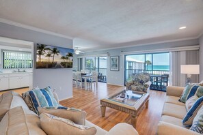 A spacious living area with a wooden floor, a sofa set, a coffee table, and a view of the ocean through large windows.