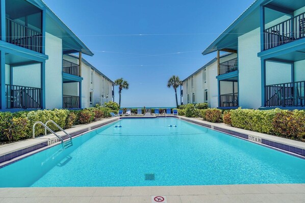 A swimming pool with a clear blue sky above, surrounded by two-story buildings with balconies.
