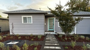 Una casa con fachada gris, una puerta verde y un pequeño jardín con piedras que conducen a la entrada.