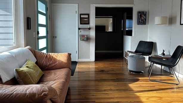 Una sala de estar moderna con un sofá de cuero marrón, un sillón gris y suelo de madera.