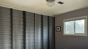 Un dormitorio con un ventanal grande, una cama y un cuadro colgado en la pared.