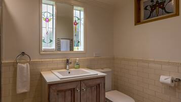 A bathroom with a white sink, wooden cabinets, a toilet, and a stained glass window above the mirror.