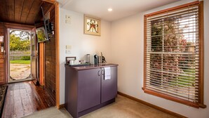 Ein Zimmer mit Holzboden, einem violetten Schrank mit Küchengeräten, einem Fenster mit Jalousien und einer zur Außenseite führenden Tür.