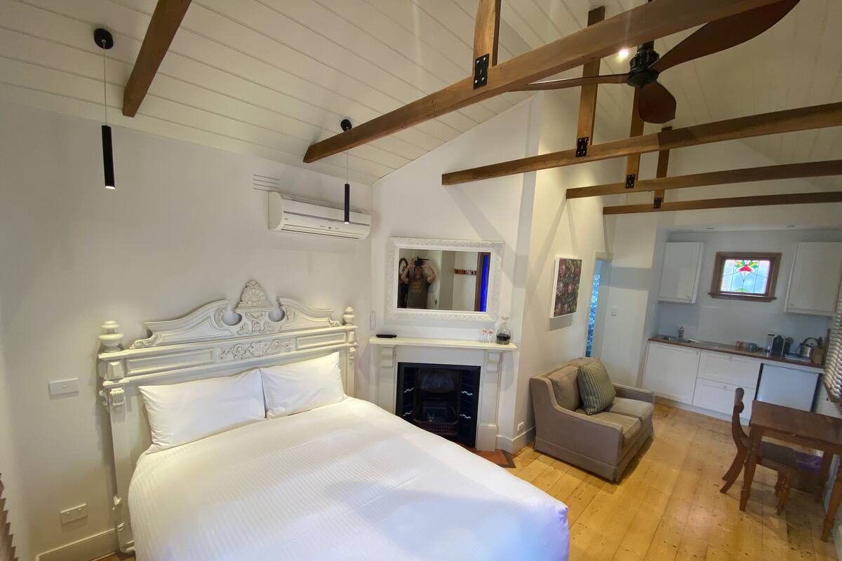 Un dormitorio con una cama grande, una chimenea, una zona de comedor y una cocina con armarios blancos.