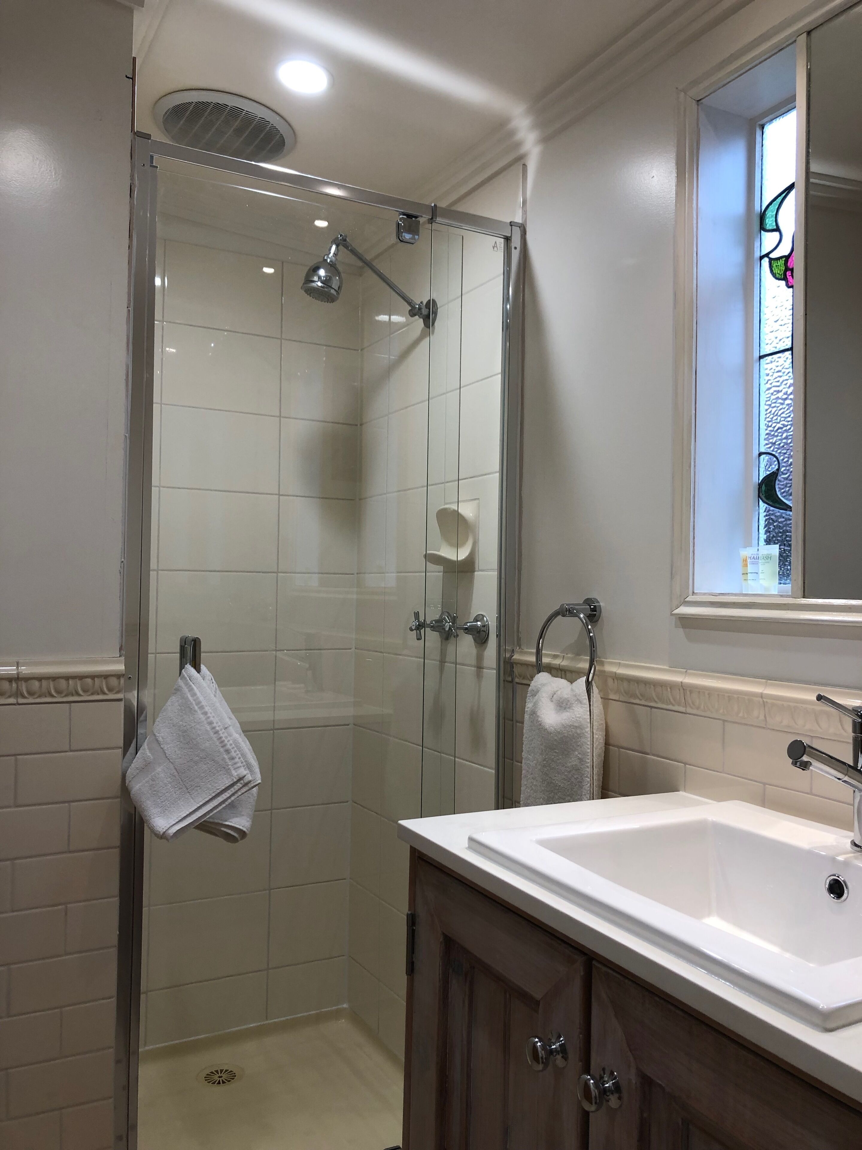 Een moderne badkamer met een douchecabine van glas, een witte wastafel en een raam met een decoratief uitzicht.