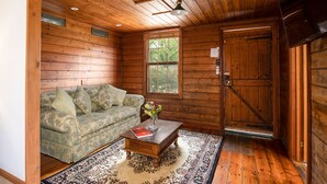 Ein gemütliches Blockhaus-Interieur mit Holzbalkendecke, einer Couch, einem Couchtisch mit Buch und Vase sowie einem großen Fenster.