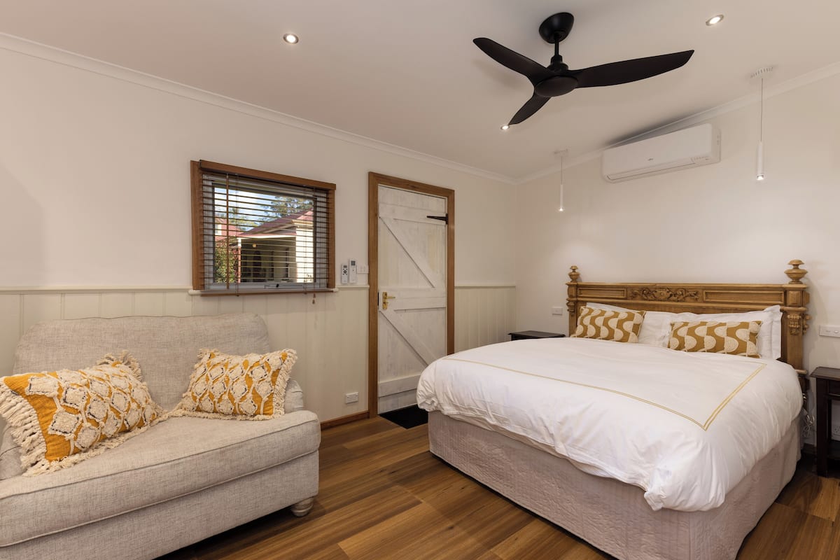 Un dormitorio con cama, sofá, ventilador de techo, equipo de aire acondicionado y ventana con persianas.