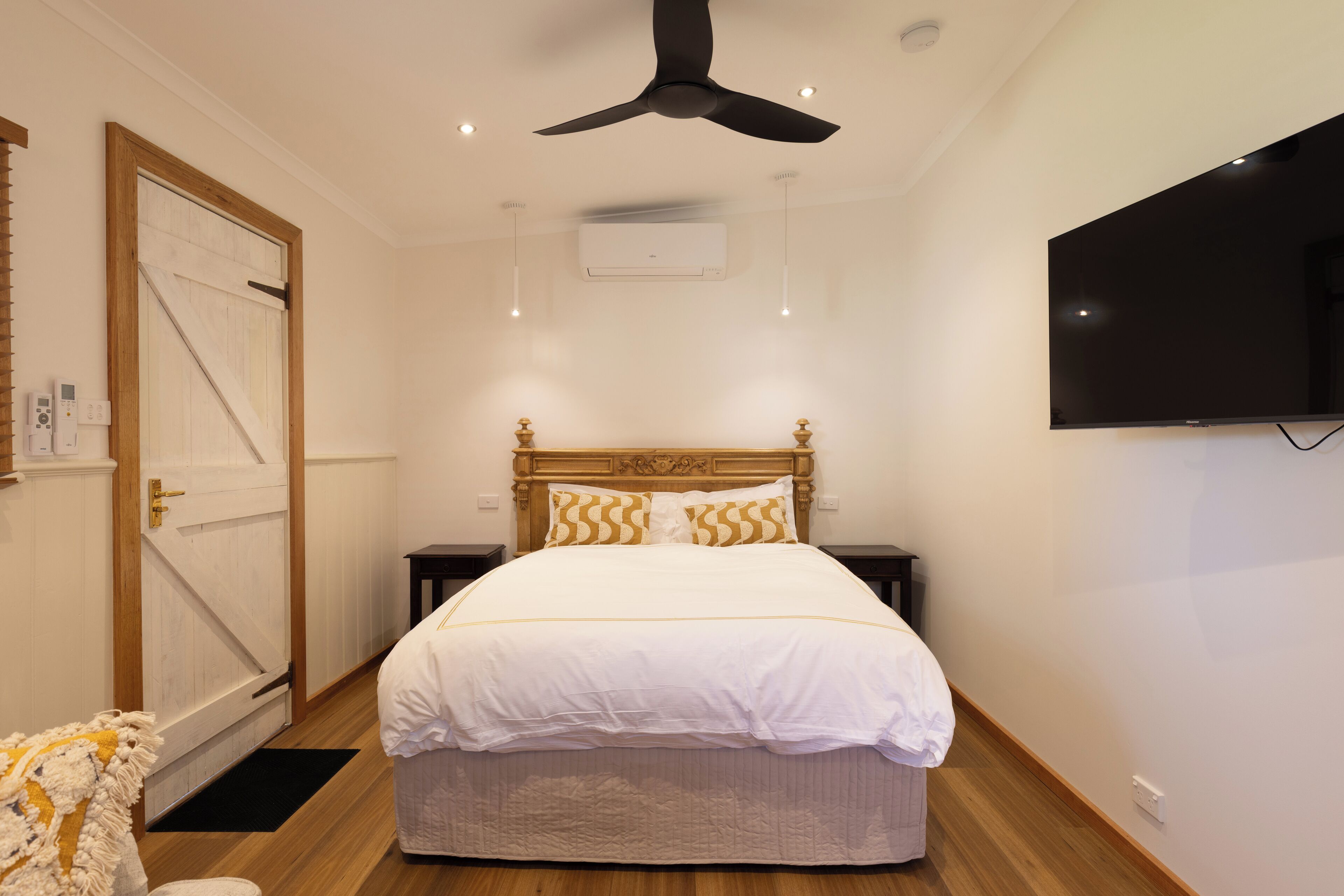 Un dormitorio con cama, ventilador de techo, equipo de aire acondicionado, televisor y puerta de madera.