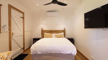 Un dormitorio con cama, ventilador de techo, equipo de aire acondicionado, televisor y puerta de madera.