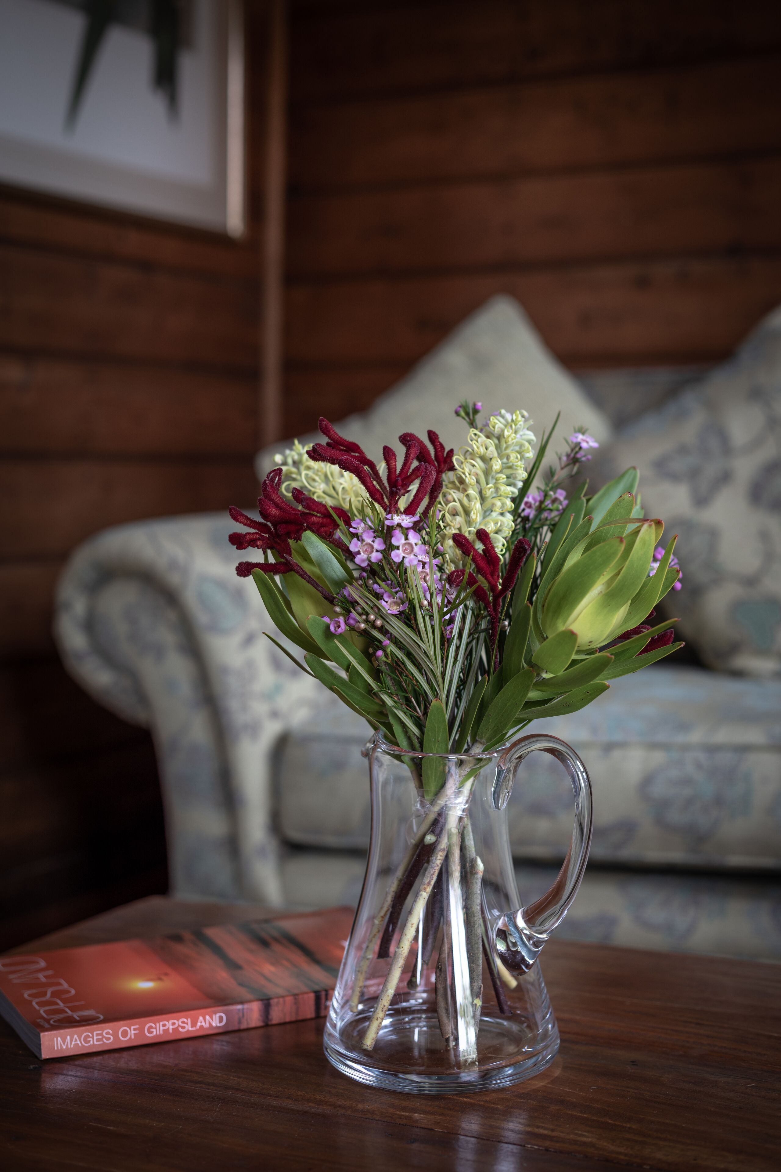Un jarrón de cristal transparente con un arreglo floral sobre una mesa de madera.
