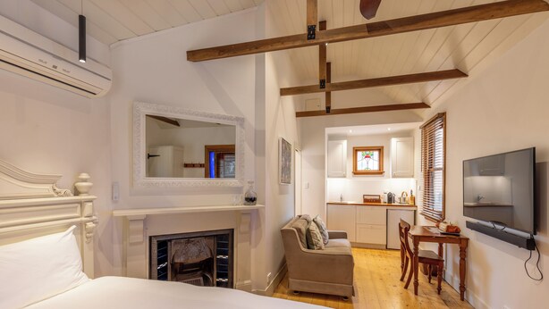 Ein Schlafzimmer mit einem großen Bett, Kamin, einer Couch, einer Essecke mit Tisch und Stühlen sowie einem an der Wand montierten Fernseher.