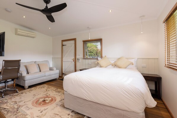 Un dormitorio con cama, una silla, ventilador de techo y ventana con persianas.