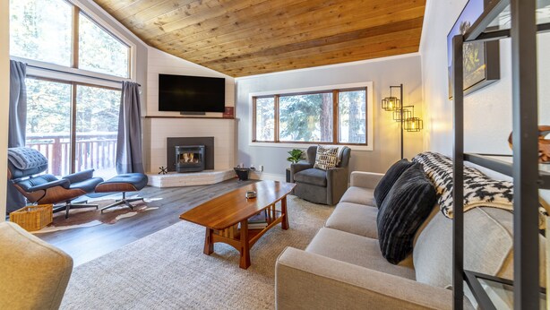 A spacious living room with a wooden ceiling, large windows, a fireplace, and modern furniture. - Newly Remodeled by Eagle Lodge; Jacuzzi & Parking (Mammoth Lakes)