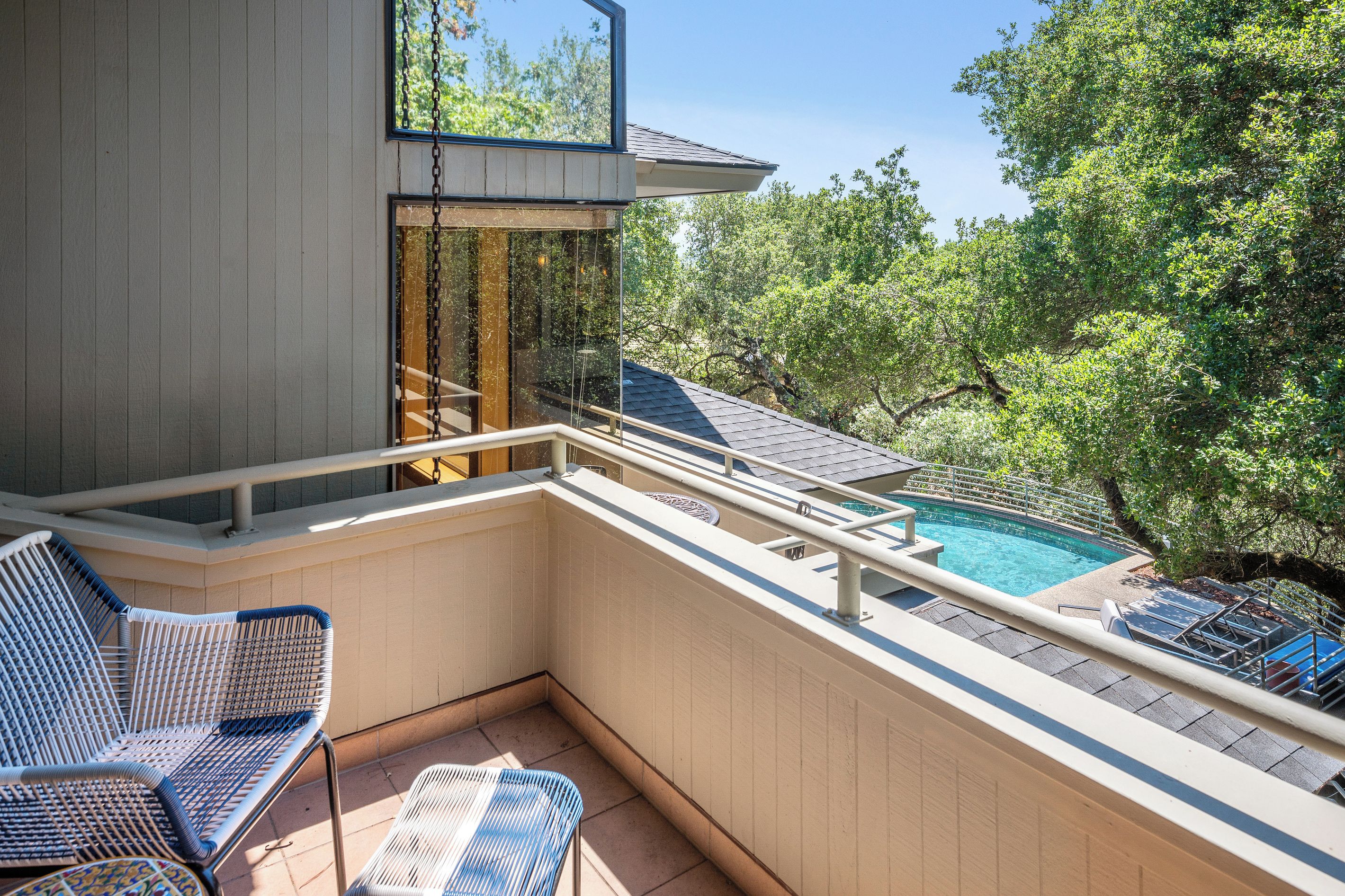 A balcony with a pool, wicker chairs, and a view of trees.