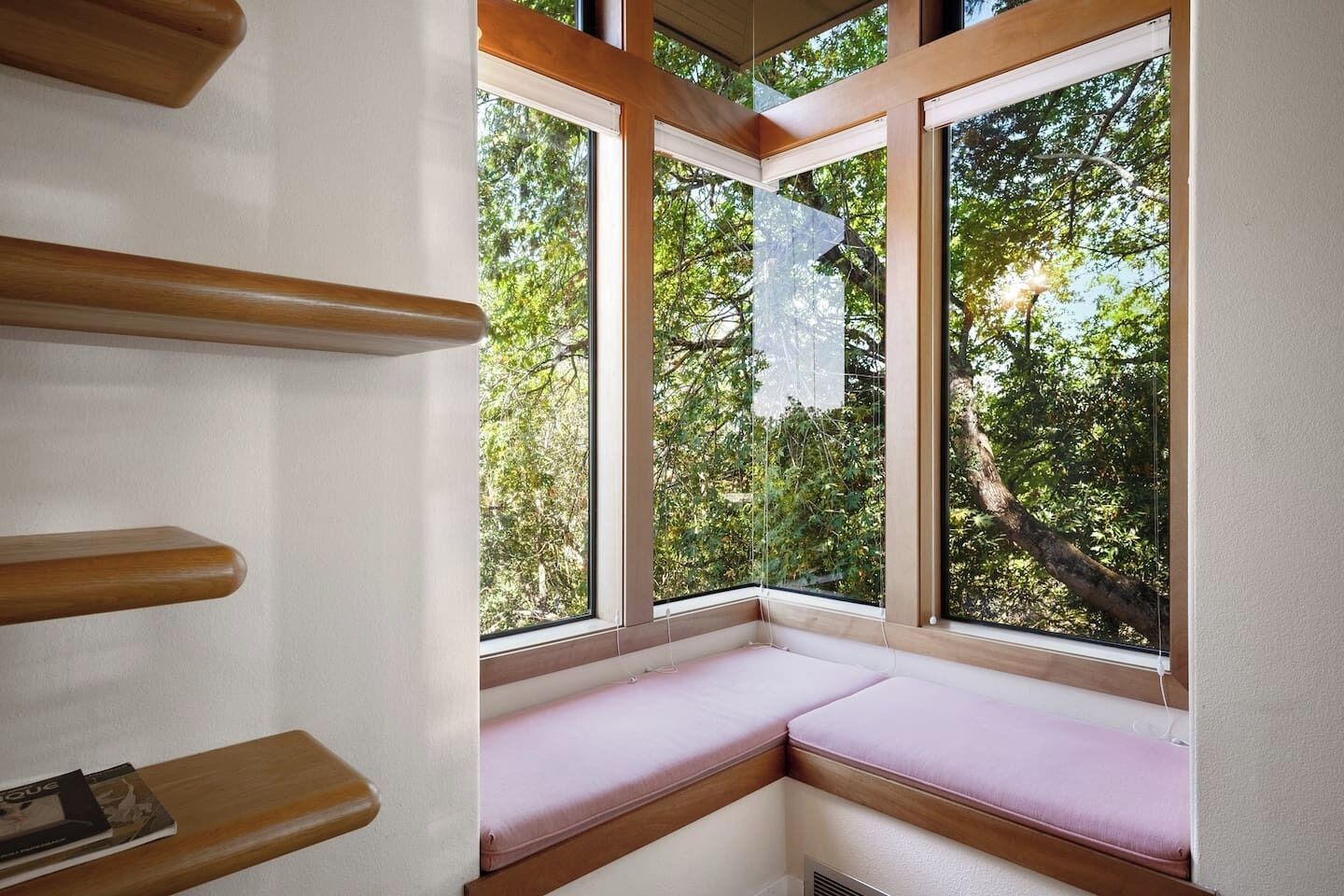 Une pièce d’angle dotée d’une banquette intégrée et d’une grande fenêtre donnant sur une zone verdoyante bordée d’arbres.