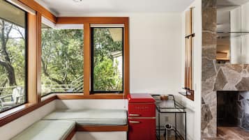 A compact kitchen with a built-in stove, a red refrigerator, and a window seat with a view of trees.