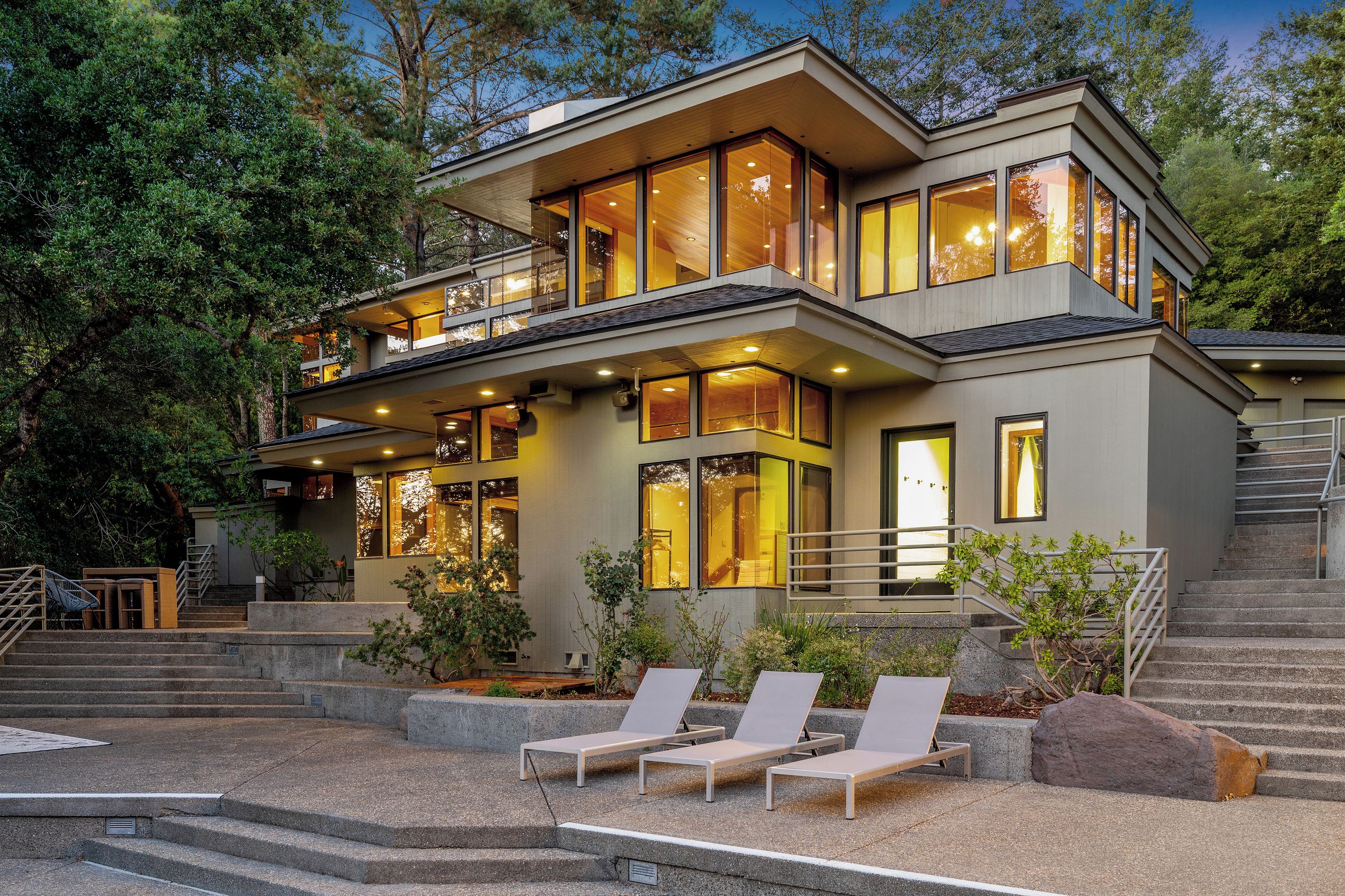 A modern two-story house with a balcony, large windows, and outdoor seating.