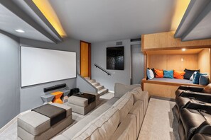A modern home theater with a large screen, comfortable seating, and a wooden loft bed.