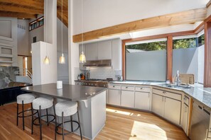 Une cuisine moderne dotée d’un îlot central, de tabourets de bar, d’une cuisinière et d’une grande fenêtre.