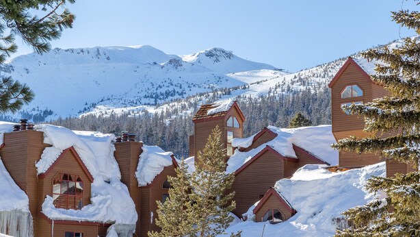 A snow-covered lodge with multiple wooden buildings, a mountain backdrop, and a clear sky. - Remodeled Retreat at Eagle Lodge - Spa & Garage! (Mammoth Lakes)