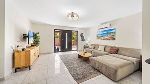 Ein modernes Wohnzimmer mit einem beigen Sofa, einem Holzschrank, einem Flachbildfernseher und einem großen Fenster.