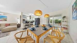 Eine moderne Küche mit Essbereich, ausgestattet mit einem großen Tisch und Stühlen, Deckenleuchten und Blick in das Wohnzimmer.