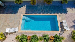 A rectangular swimming pool with a tiled deck, surrounded by lounge chairs and palm trees. - Great Cozy, Comfortable & Central 2BR 2BA w/ Pool (Noord)