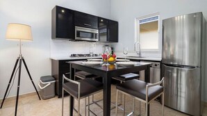 A modern kitchen with black cabinets, stainless steel appliances, a dining table with chairs, and a floor lamp. - Great Cozy, Comfortable & Central 2BR 2BA w/ Pool (Noord)