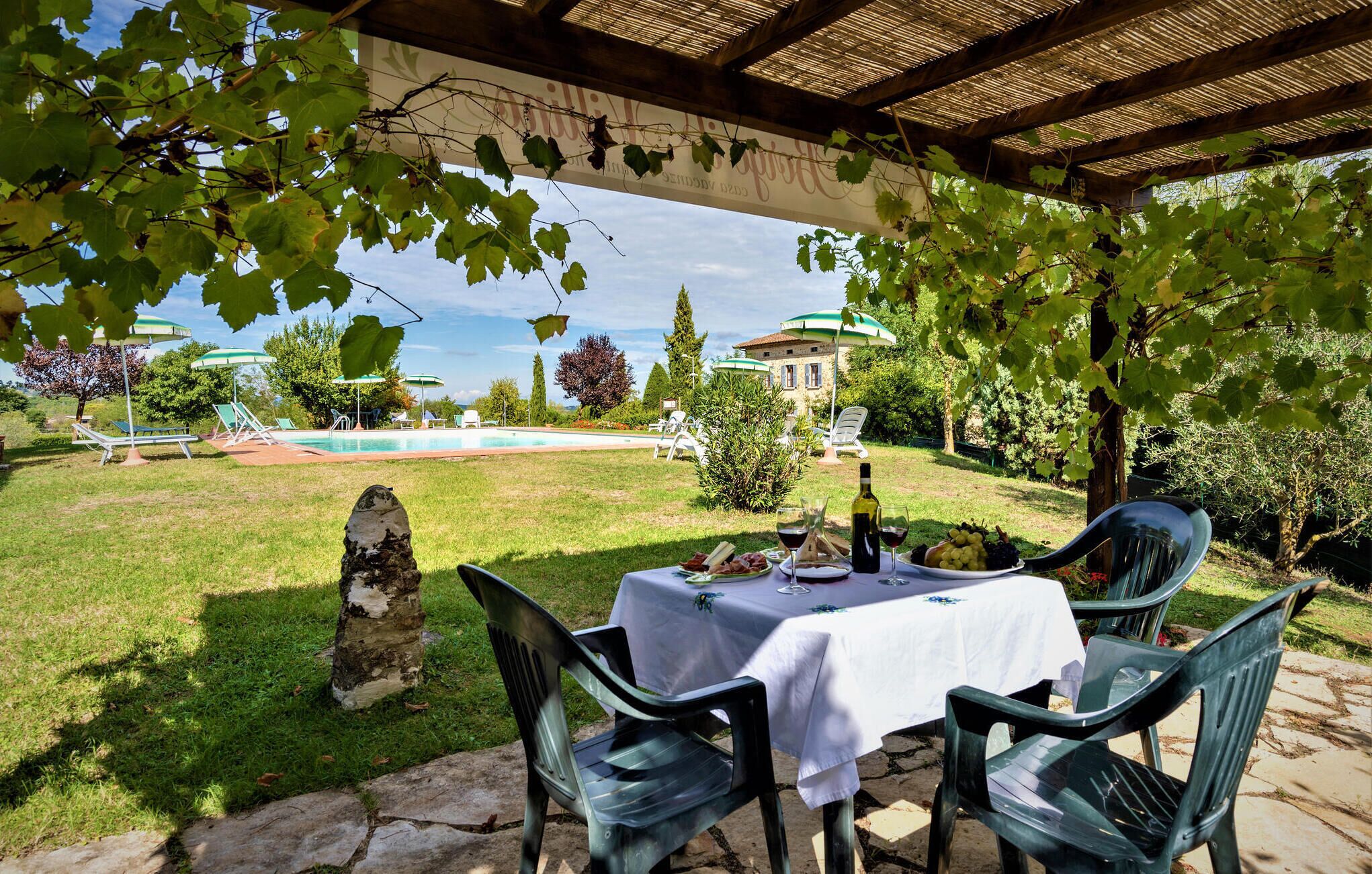 Ein Essbereich im Freien mit einem Tisch für zwei Personen, umgeben von Grün und Blick auf Pool und Villa im Hintergrund.