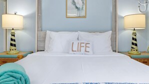 A neatly made bed with white linens, a pillow with the word "LIFE" on it, and two nightstands with lamps and a small lighthouse decoration. - Spacious 1-bed w/ courtyard near Palm Beach (Palm Beach)