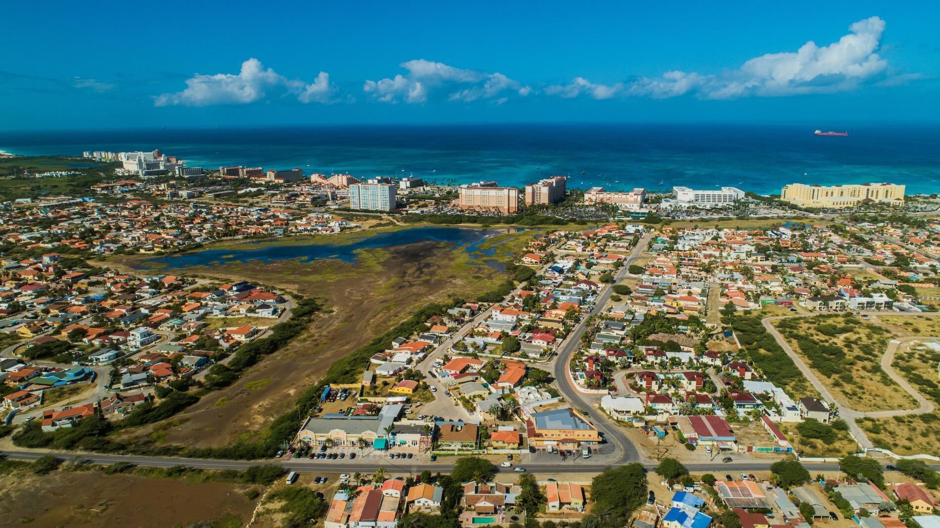 Vista aérea de un pueblo costero con zonas residenciales, una gran masa de agua y un puerto deportivo con barcos.