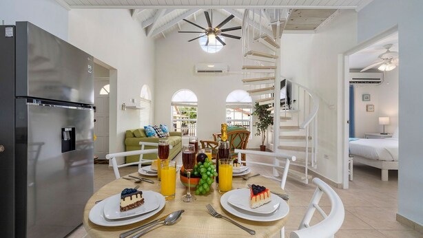 A modern kitchen with a dining table set for breakfast, a refrigerator, and a staircase leading to another room. - Cute & Cozy 3BR, Great Location (Noord)