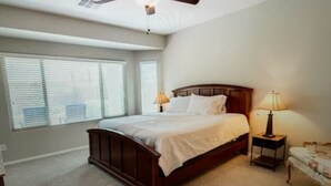 Une chambre à coucher avec un grand lit, deux tables de chevet avec des lampes et une fenêtre avec des stores.