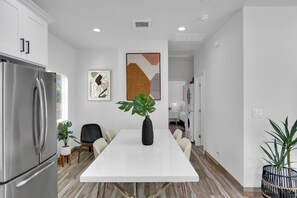 Una cocina moderna con un refrigerador de acero inoxidable, una mesa de comedor blanca y una planta en maceta.
